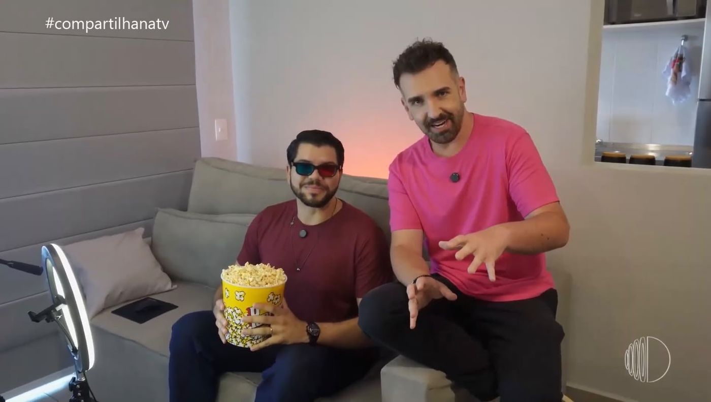 Cena de gravação da reportagem do Compartilha, com dois homens num sofá e um balde de pipoca